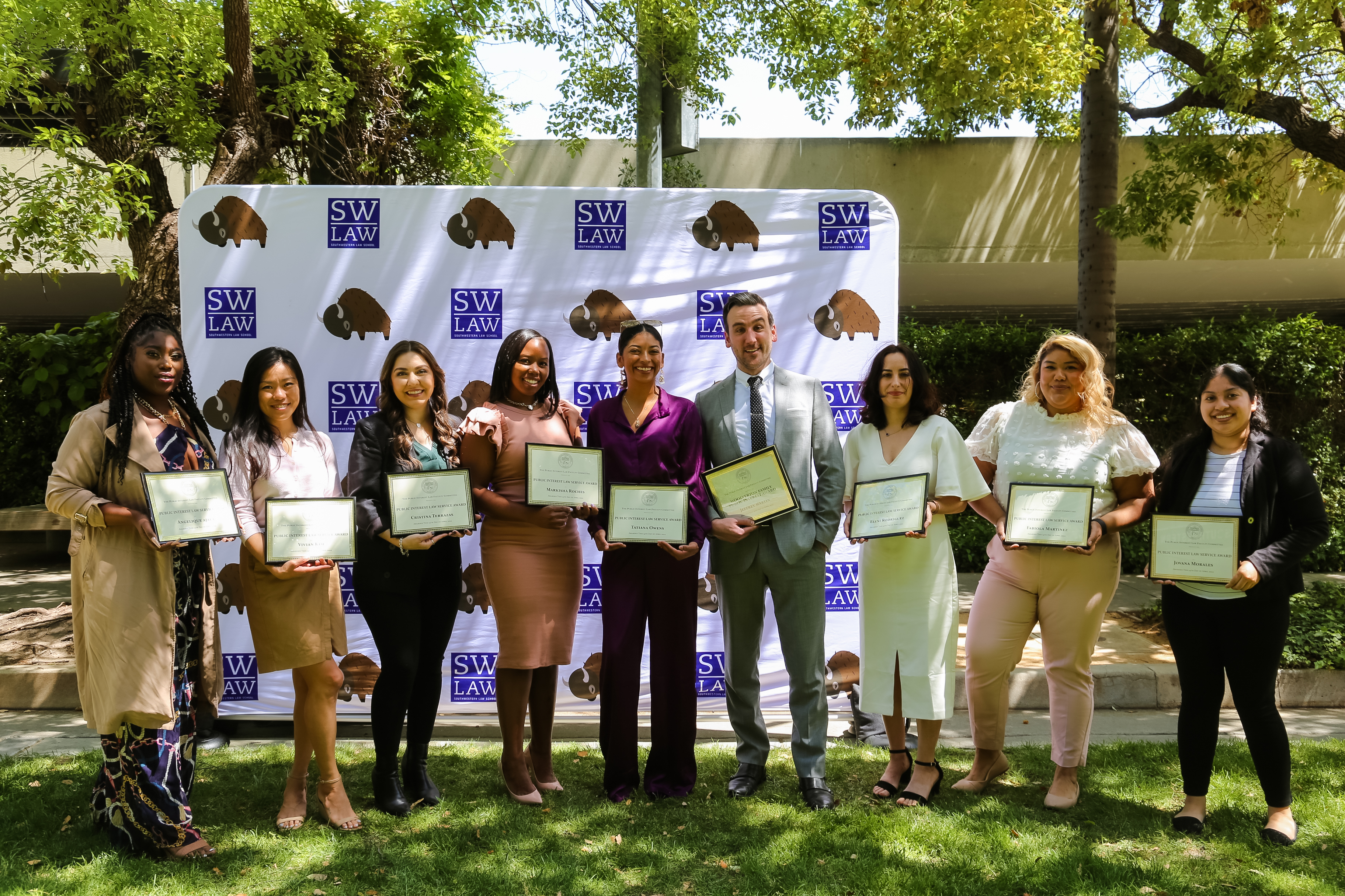 Nine Southwestern Graduating Student Award recipients holding award certificates in front of SWLAW step and repeat with purple SWLAW logo and Bison mascot 