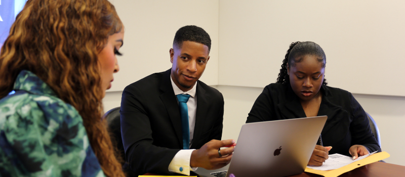 Three students in professional wear having a discussion around the table