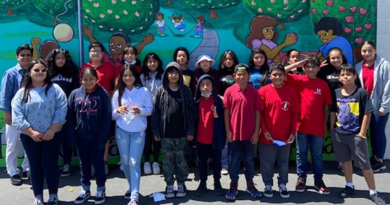 Class photo of Hoover Elementary students in two rows outside in front of a colorful mural