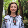 Professor Iryna Zaverukha in a traditional Ukrainian embroidered blouse standing in front of green foliage 