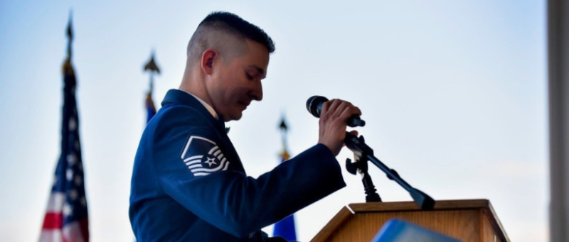 Jordan Herrera in uniform at podium with flags in the background