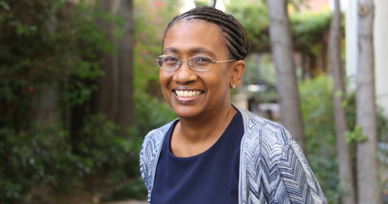 Professor Thompson-Bell headshot smiling at camera against greenery