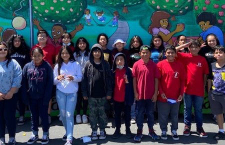 Class photo of Hoover Elementary students in two rows outside in front of a colorful mural
